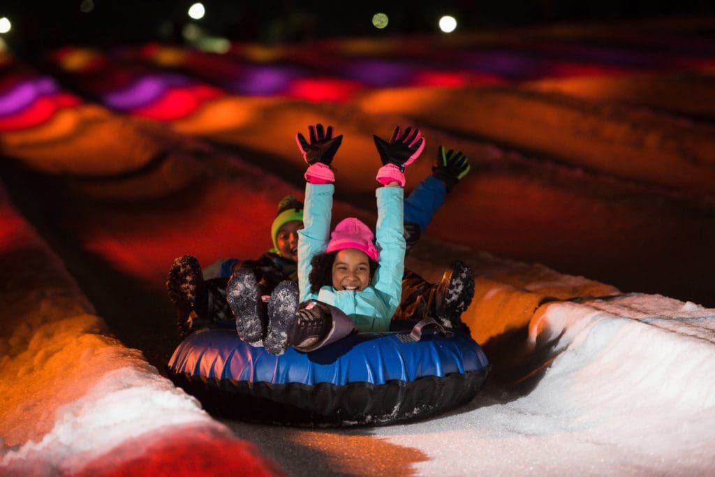 Two kids tandem snow tube down a run at Camelback Mountain Resort.