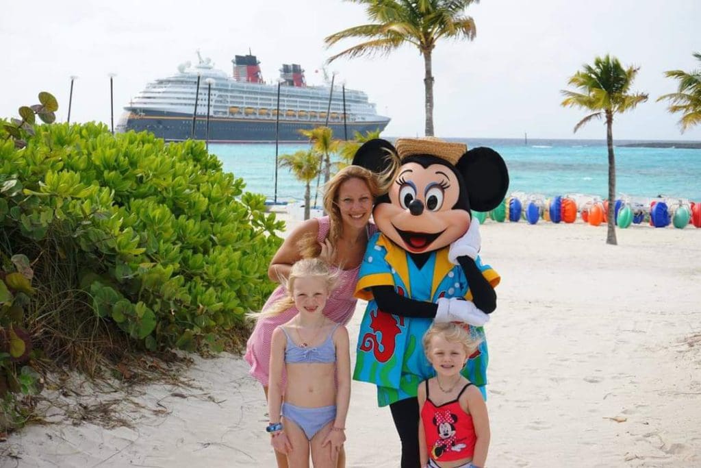 A mom and her two kids stand with Minnie Mouse on the beach, as part of a Disney Cruise, one of the best cruise lines for families.