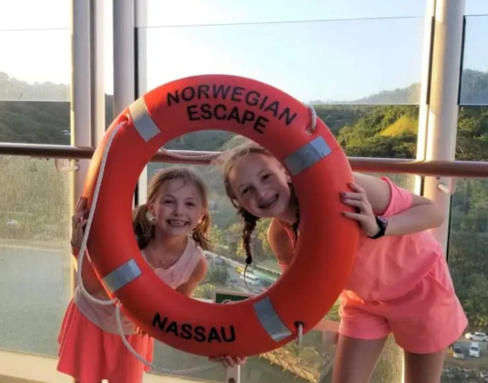 Two kids look through an orange floatation device while sailing with Norwegian cruises.