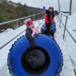A young girl carries a blue snow tube up a hill to go snow tubing at Camelback Resort with her family