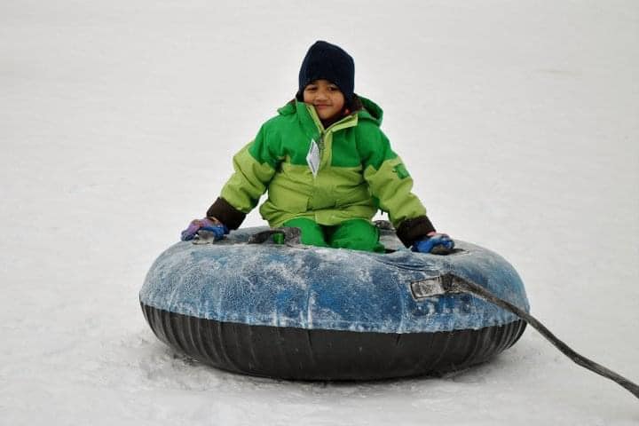 A young boy wearing a green snow jacket rides down a wintery hill on a snow tube.