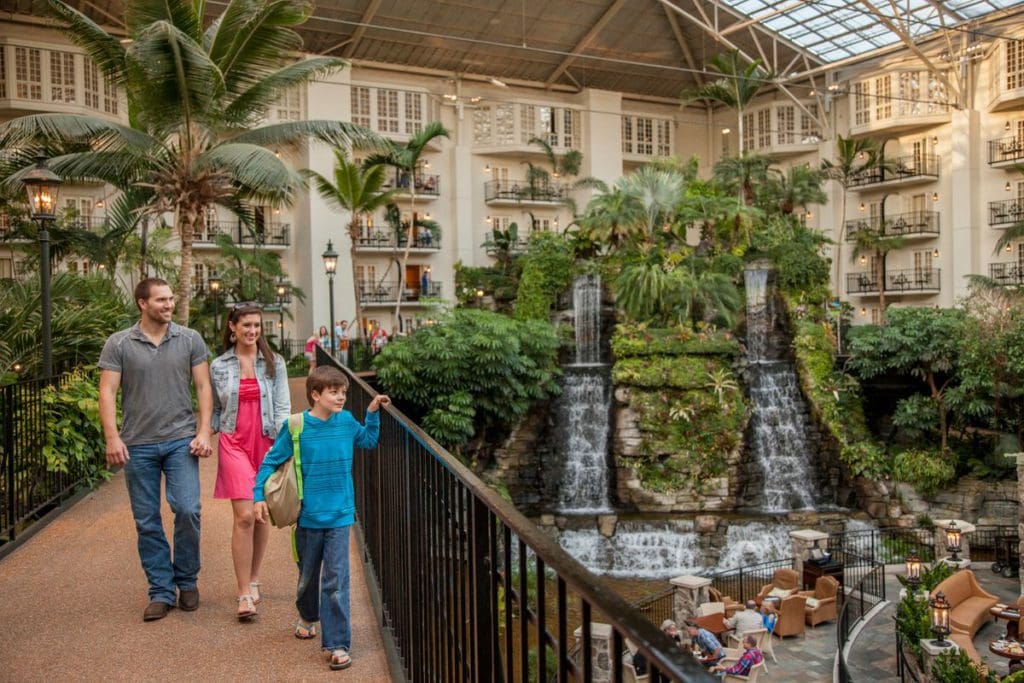 Two parents and their young son walk across the boardwalk within the atrium at the Gaylord Opryland Resort & Convention Center, with an indoor waterfall in the distance, one of the best Nashville hotels for families.