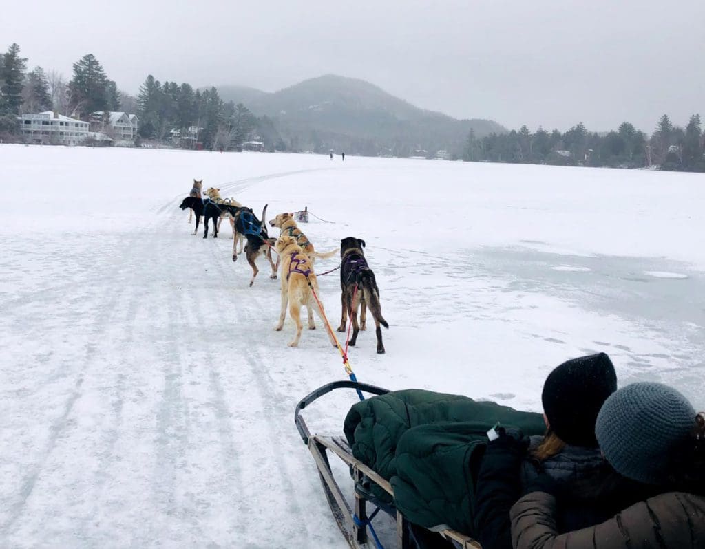 Two kids sit in a dog sled, while several dogs run the sled across Mirror Lake, near Lake Placid.