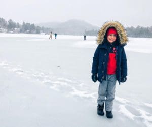 A young boy in a winter coat stands on a frozen lake in Lake Placid.