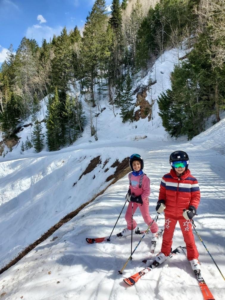 Two kids in full ski gear and skis move along a trail on Aspen Mountain.