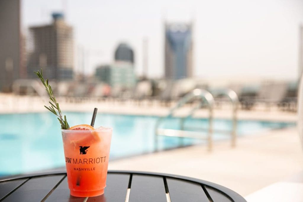 A cup reading "The JW Marriott Nashville" sits on a poolside table, with the outdoor pool behind it, one of the best Nashville hotels for families.