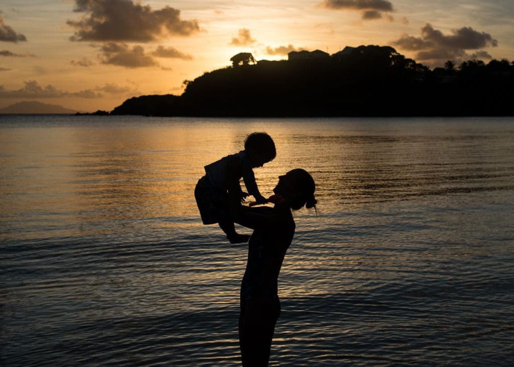 A mom holds up her young son at sunset while exploring Antigua together.