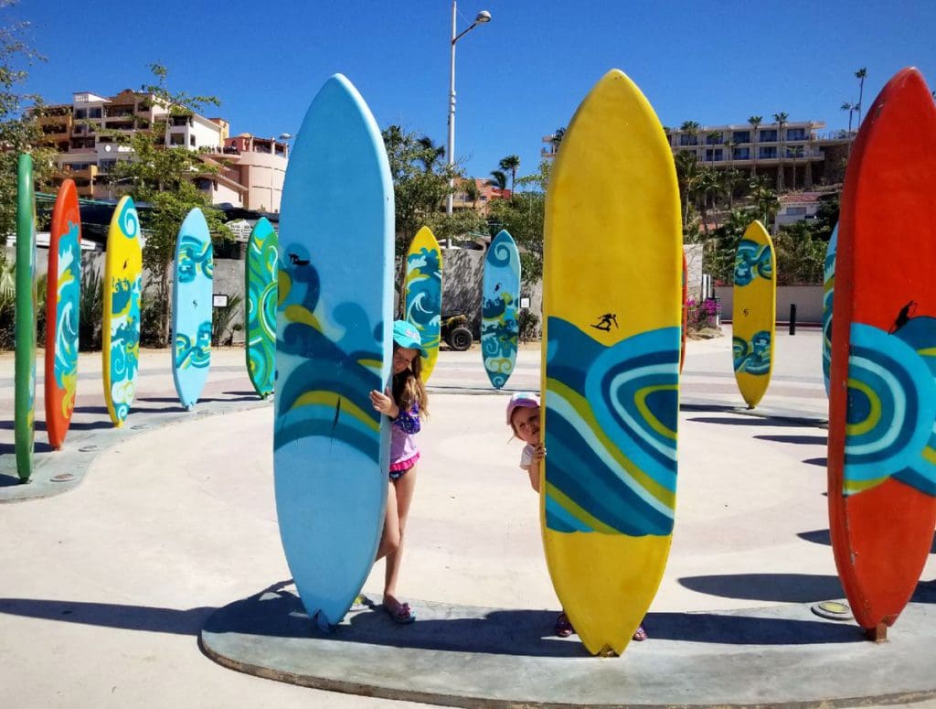 Two girls stand behind upright surf boards on a sunny day at the beach.