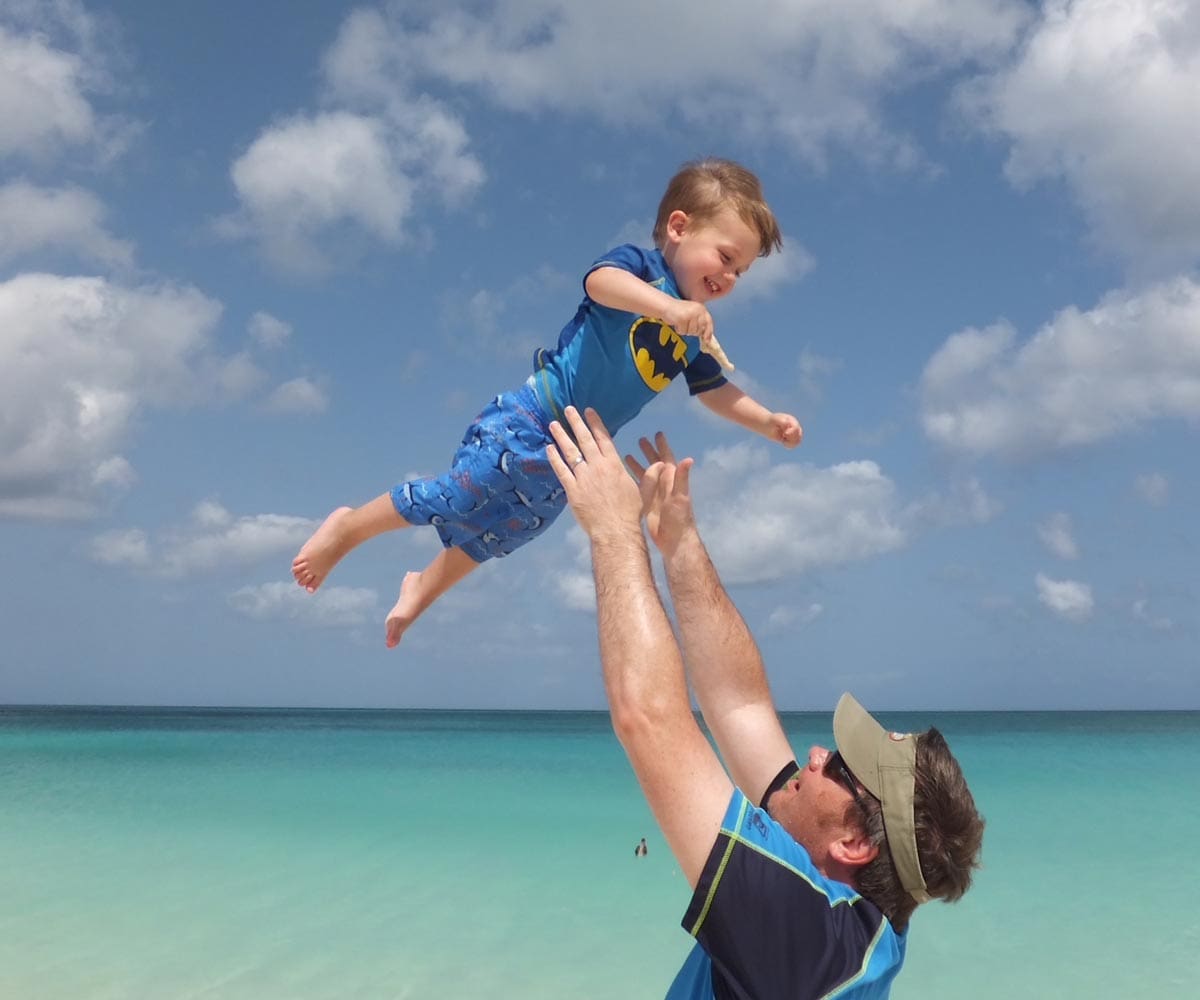 A dad throws his young son in the air, while enjoying a beach day at Eagle Beach in Aruba.