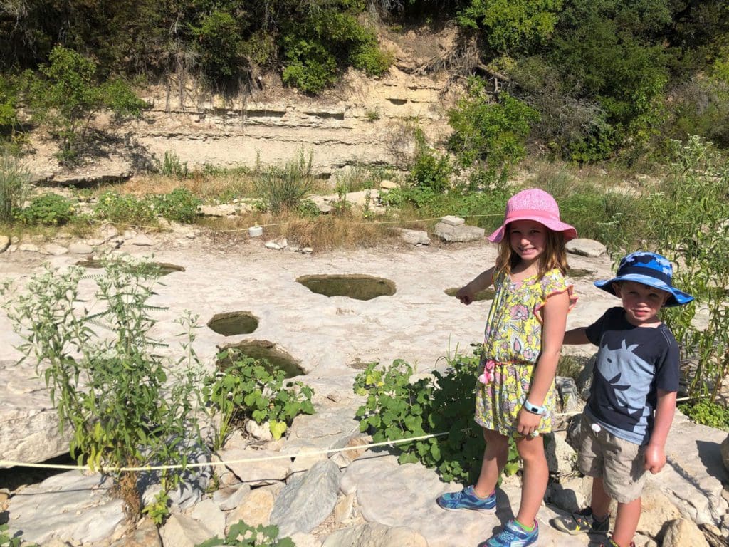 Two kids stand near an area with fossilized dinosaur prints at Dinosaur Valley State Park in Texas.
