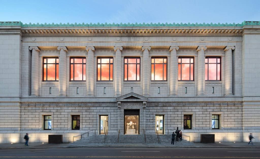 The exterior of the New-York Historical Society, with a clear view of the lit entrance at dusk.