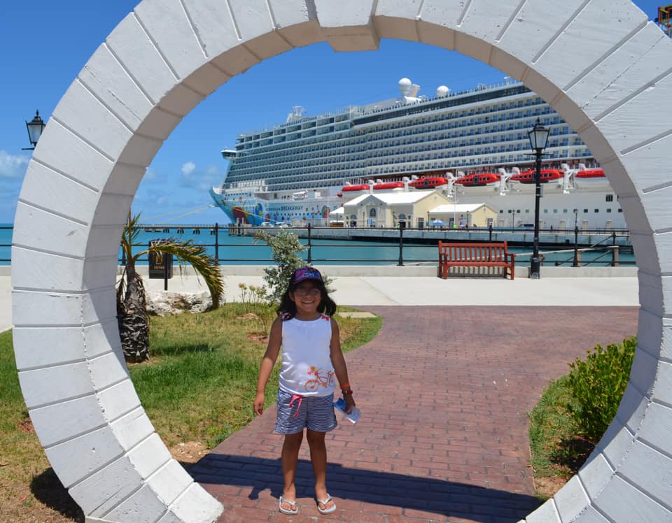 A young girl stands at the port entrance for a Norwegian Cruise on a sunny day. 