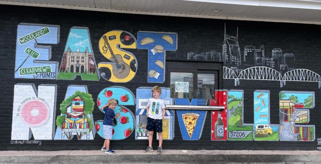 Two boys stand against a wall of street art reading "East Nashville".