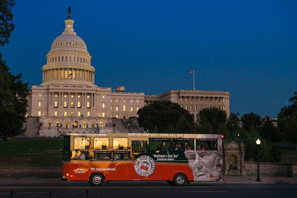 A trolley tour passes the capitol building lit up at night, as part of a Monuments by Moonlight Tour.