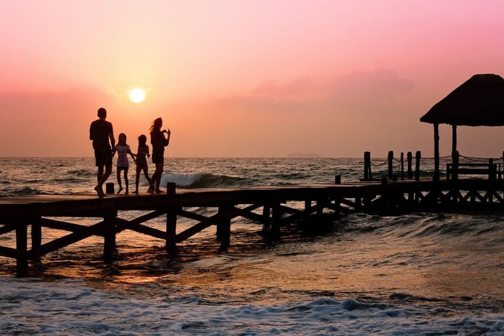 A family of four walks across a boardwalk during a beautiful sunset at the ocean.