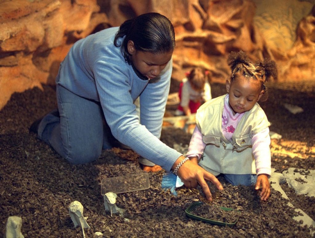 An African American mother and her daughter play in an exhibit dig site at the Chicago Children's Museum in Chicago, one of the best places to visit with your young daughter in America.