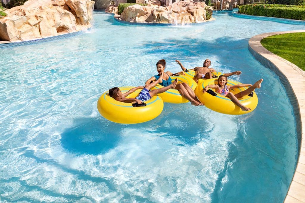 A family of four, all sitting in their own yellow tubes, float down the lazy river at Hilton Rose Hall Resort & Spa.