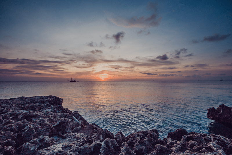 A view of a rocky shoreline at Malmok Beach, featuring a stunning sunset over the water.