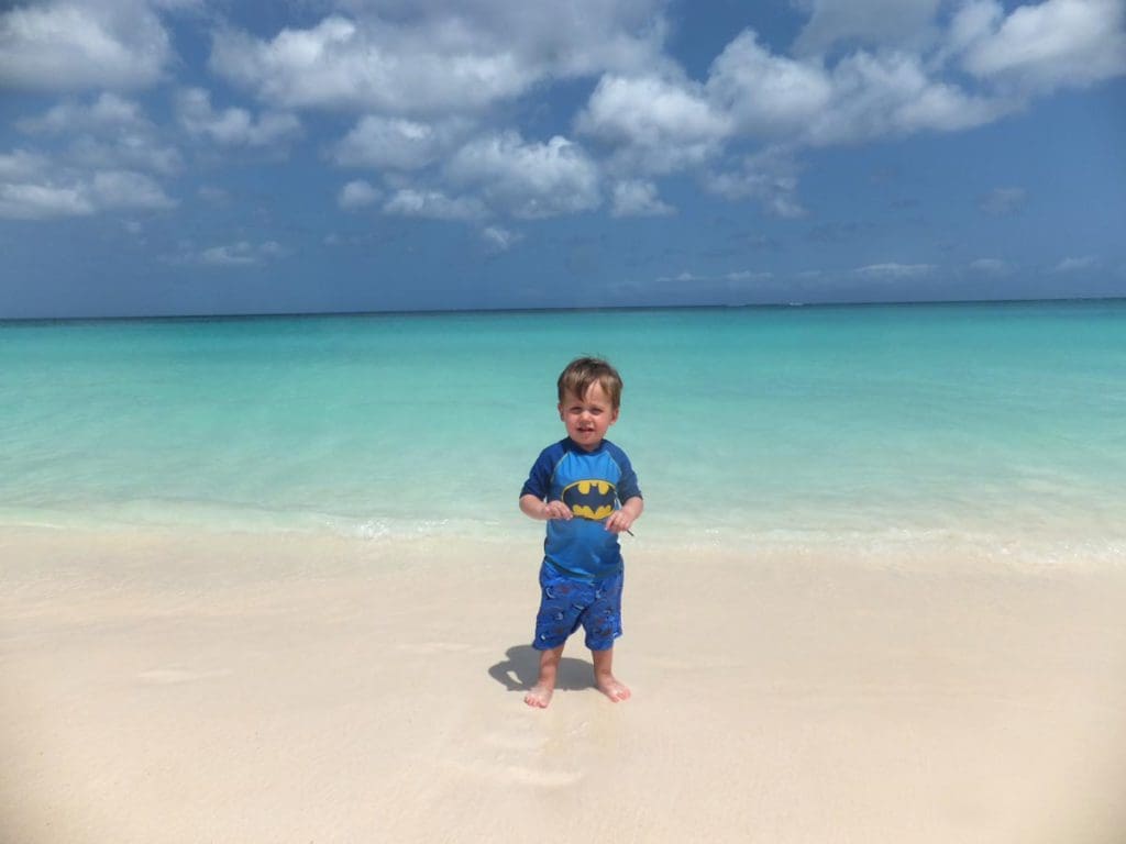 A toddler stands on Eagle Beach, one of the best beaches in Aruba for families.