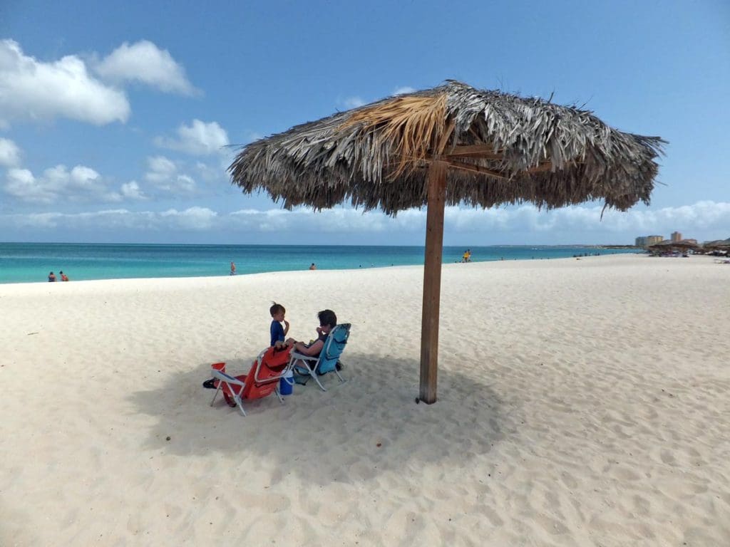 A dad sits on a beach lounger, while watching his kids play on Eagle Beach, one of the best beaches in Aruba for families.