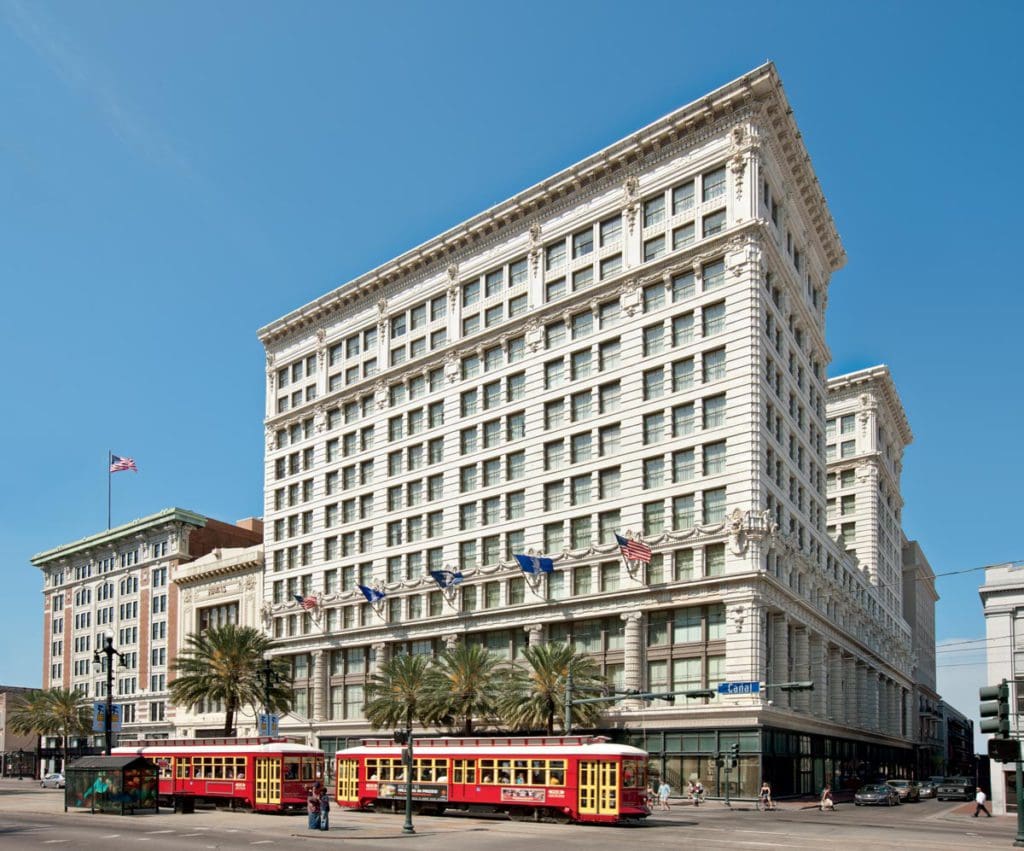 The exterior of The Ritz-Carlton New Orleans, featuring two trolleys parked outside the entrance on a sunny day at one of the best hotels in New Orleans for families.
