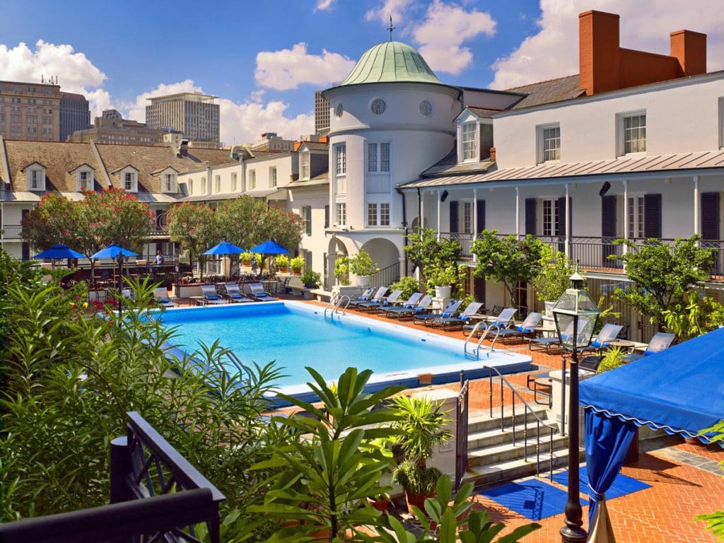 The outdoor pool at Royal Sonesta New Orleans, featuring a rooftop view, stunning pool deck with swaying palms, and cabana seating.