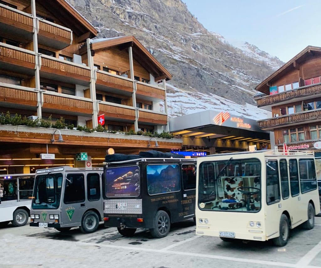 Several electric busses are lined up on a street in Zermatt.