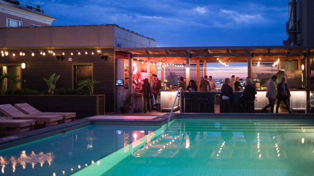 The rooftop pool at Ace Hotel at night, with a group of people enjoying time at the outdoor bar behind it.