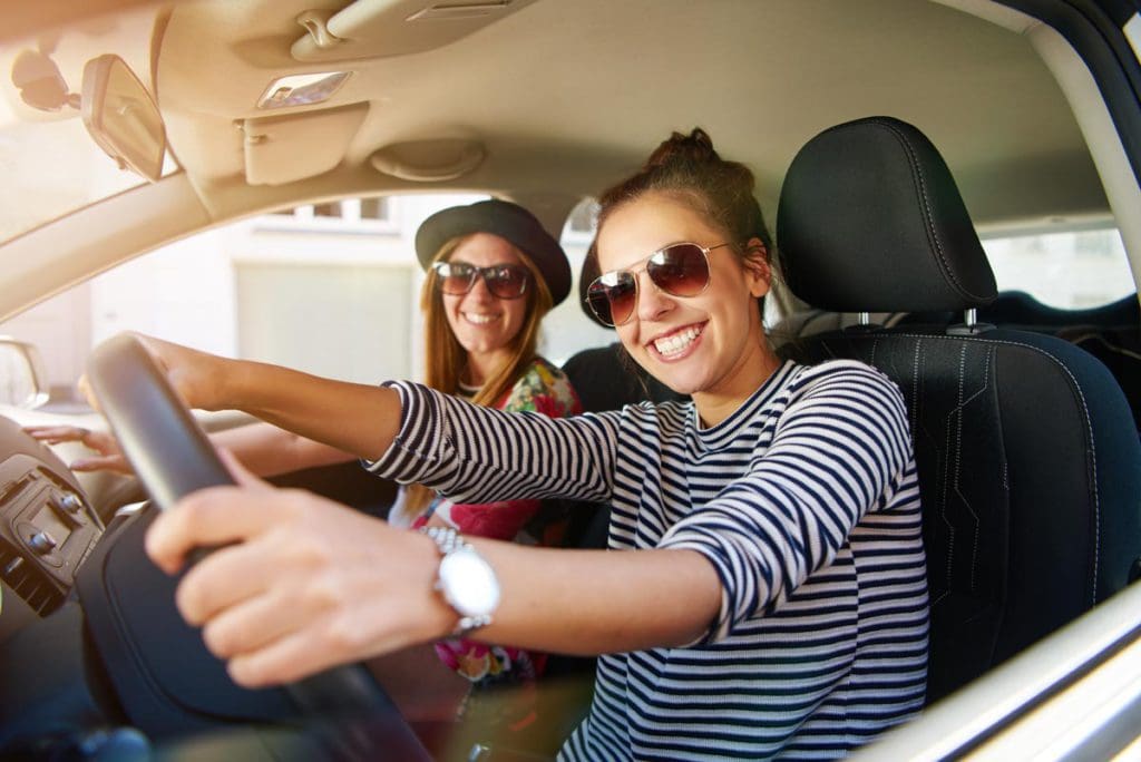Two woman sit in the front seat of a car, while on a girls' trip.