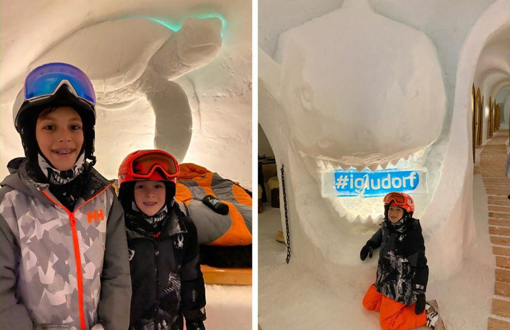 Left Image: Two kids in full snow gear stand together in front of a sea turtle carved from the snow at the Igloo Village. Right Image: A young boy in full snow gear sits in front of a lit sight for the Igloo Village in Switzerland.