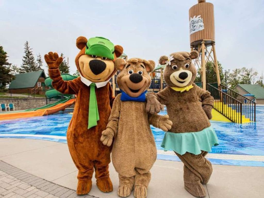 Three Yogi Bear mascots stand in front of a water park at Jellystone Park in Western New York, one of the best themed hotels in the United States for families.
