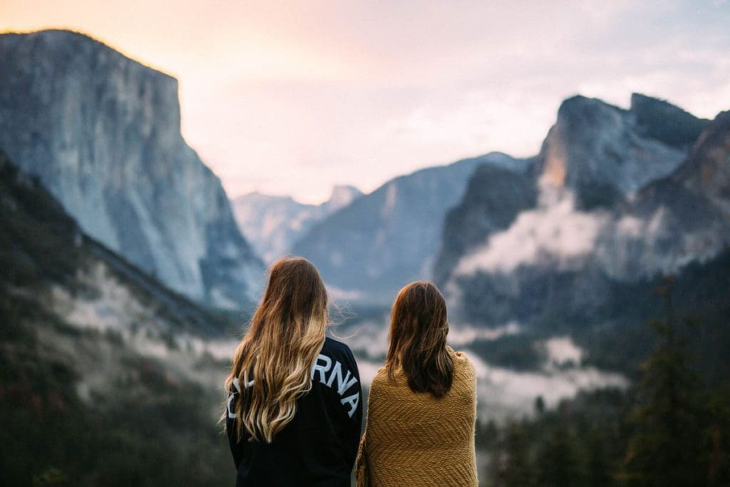 Two women stand close together looking at a view of the mountains.