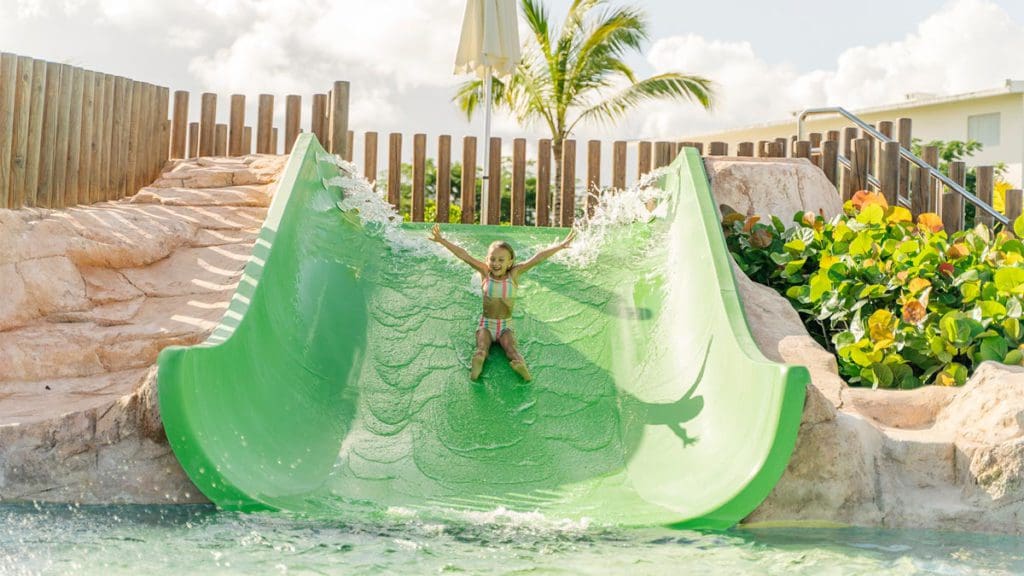 A young boy slides down a green slide at an outdoor pool at Nickelodeon Resort Punta Cana, one of the best all-inclusive resorts in the Caribbean for families.
