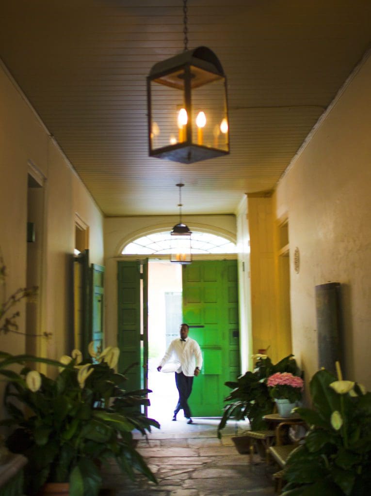 Inside one of the hallways of the Soniat House Hotel, with a staff member rounding the corner to walk down the hallway.