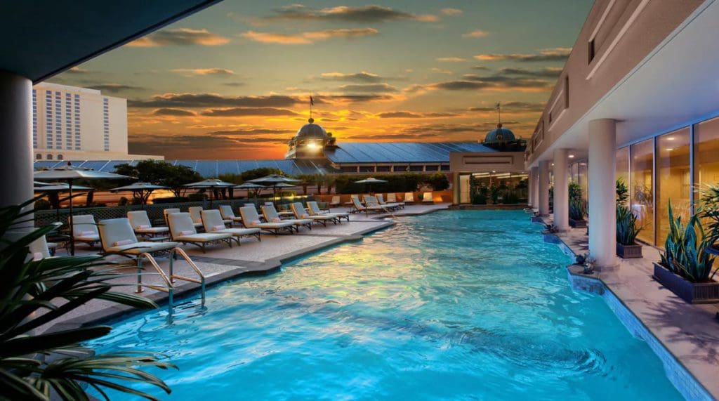 The terrace pool at Windsor Court Hotel, with a line of poolside loungers facing the pool, and a beautiful sunset overhead.