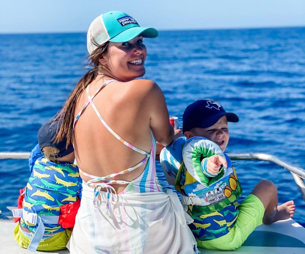 A woman sitting on a boat turns around laughing, while her two kids sit in front of her, and the ocean beyond. This is in Costa Rica, one of the best places to visit with kids in 2024. 