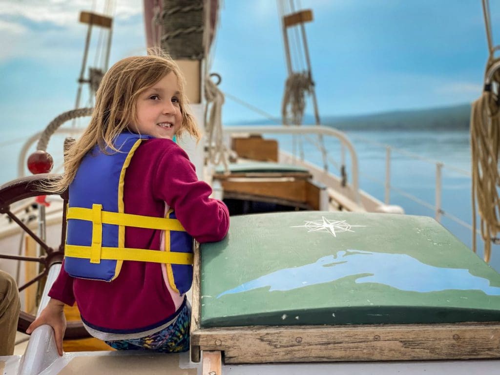 A young girl wearing a life jacket smiles as she sails along Lake Superior in a schooner, off-shore from Grand Marais, Minnesota, one of the best cool-weather destinations in the United States for families.
