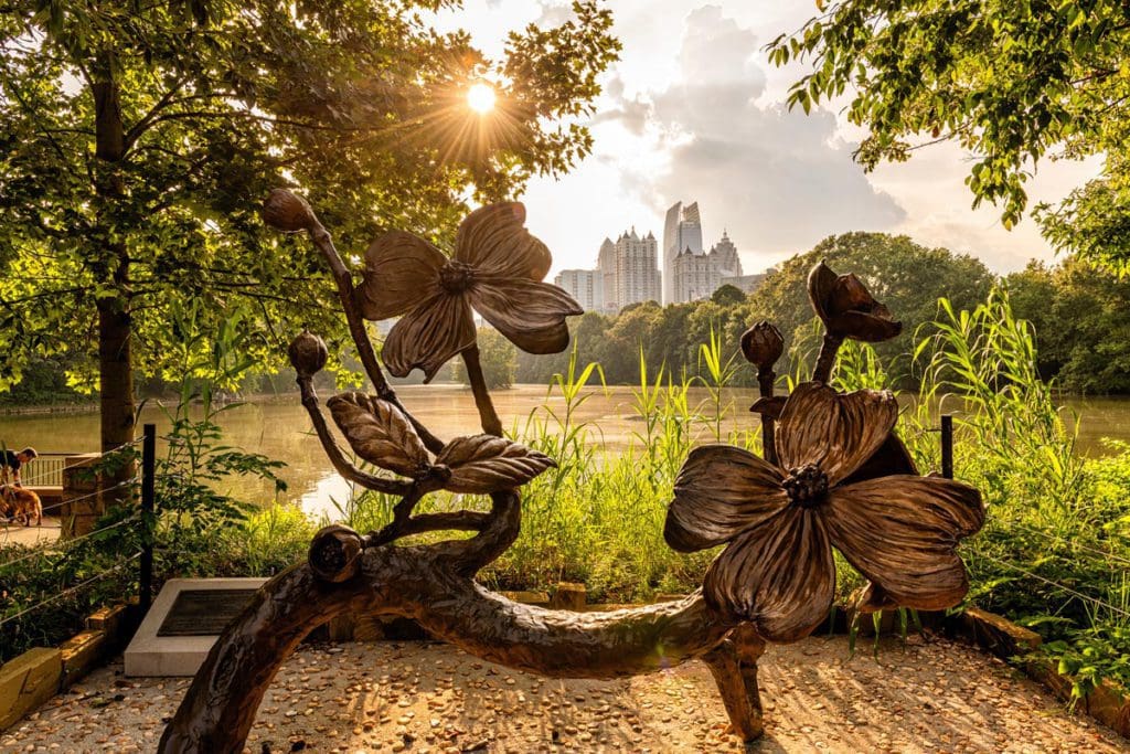 A flower statue installation at Piedmont Park in Atlanta with the sun shining down on it and the Atlanta skyline in the distance.
