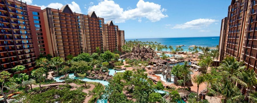 An aerial view of Aulani, A Disney Resort & Spa, featuring huge resort buildings, pools, palm trees, and an ocean view.