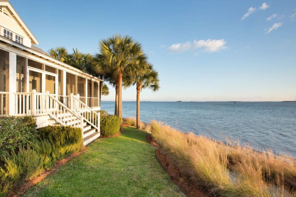 One of the seaside cottages at The Cottages on Charleston Harbor, featuring lush foliage between the house and sea.