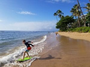 A young boy boogie boards along an oceanfront in Hawaii.