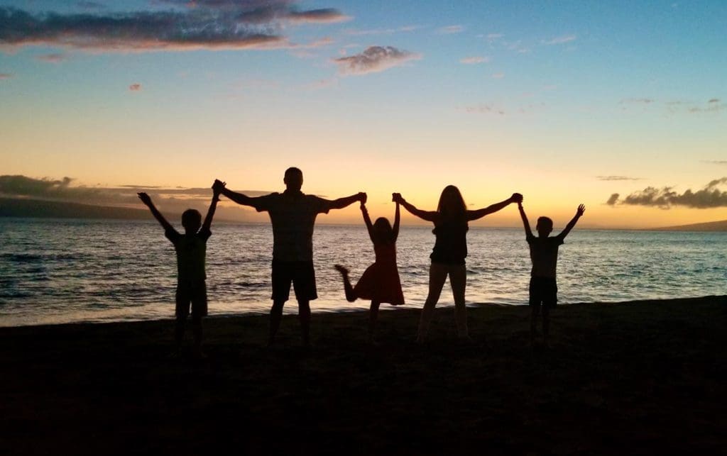 A family of five stands against a sunset in Hawaii as shadowed figures.