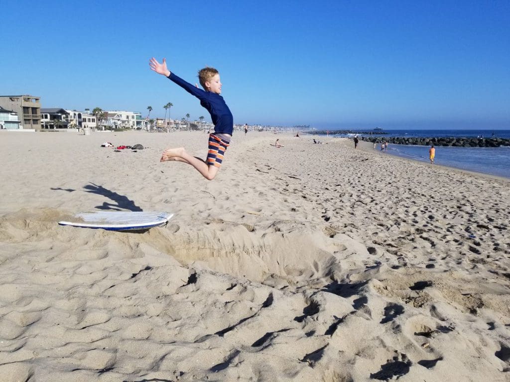 A tween boy jumps from the sand near the ocean in LA.