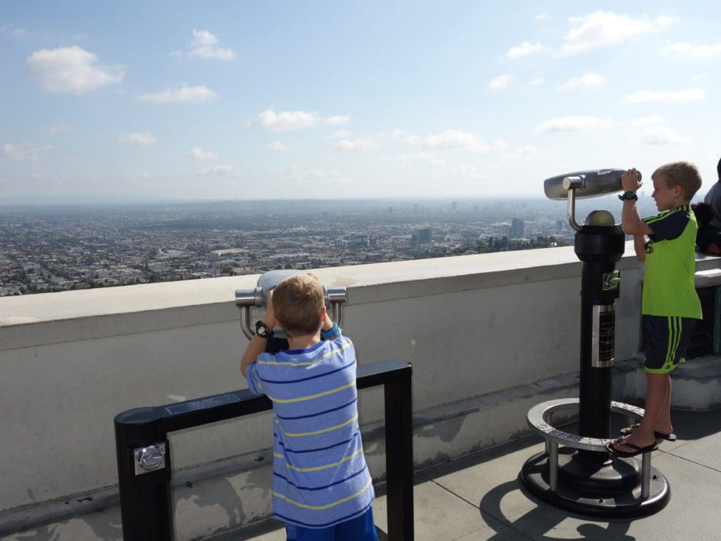 Two tween boys look through observation viewers on top of the Griffith Observatory in LA, one of the best things to do in Los Angeles with teens this summer. 