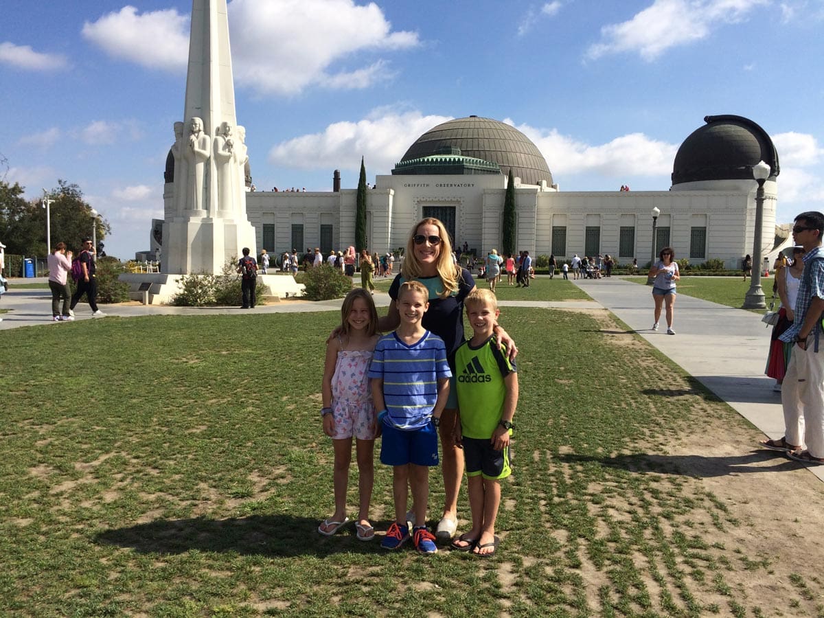 A mom and her three kids stand outside the front exterior of the Griffith Observatory on a sunny day, one of the best things to do in LA with teens.