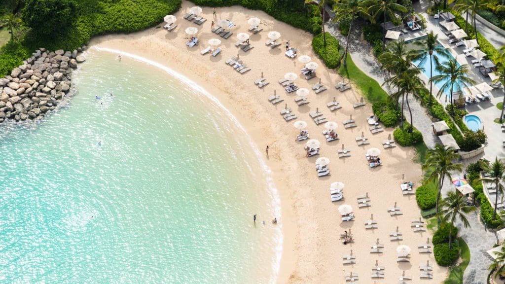 An aerial view of the pristine beach and lined beach cabanas at Four Seasons Resort O'ahu Ko Olina, one of the best resorts for families in O'ahu.