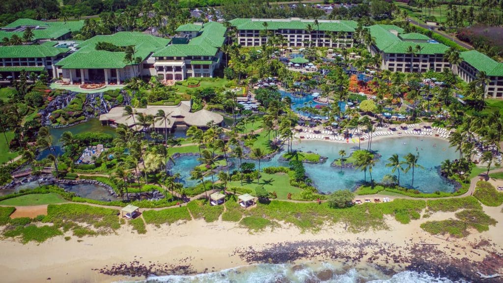 An aerial view of Grand Hyatt Kauai Resort & Spa, featuring a long beach shore, resort buildings, and pools.