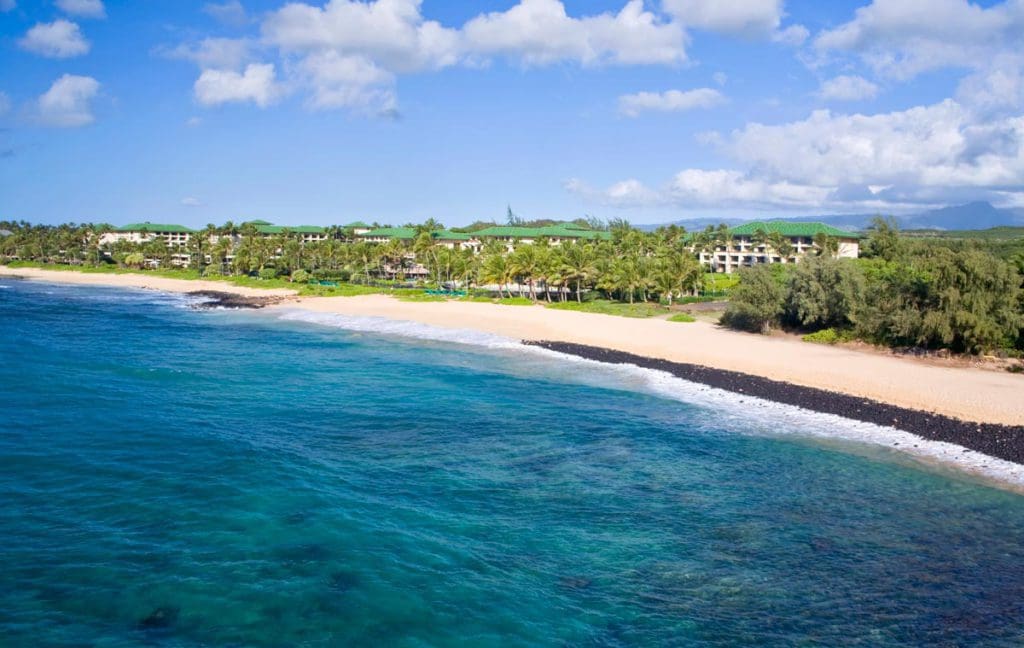 The long, stunning beach shore of Grand Hyatt Kauai Resort & Spa, featuring beautiful sand and blue waters at one of the best hotels in Hawaii for a family vacation.