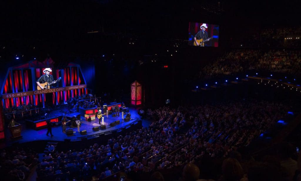 Brad Paisley singing on stage at Grand Ole Opry, with a full audience enjoying the concert.