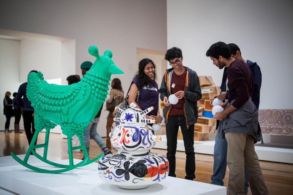 Several teens enjoy an art installation of a green chicken-figure at High Museum of Art.
